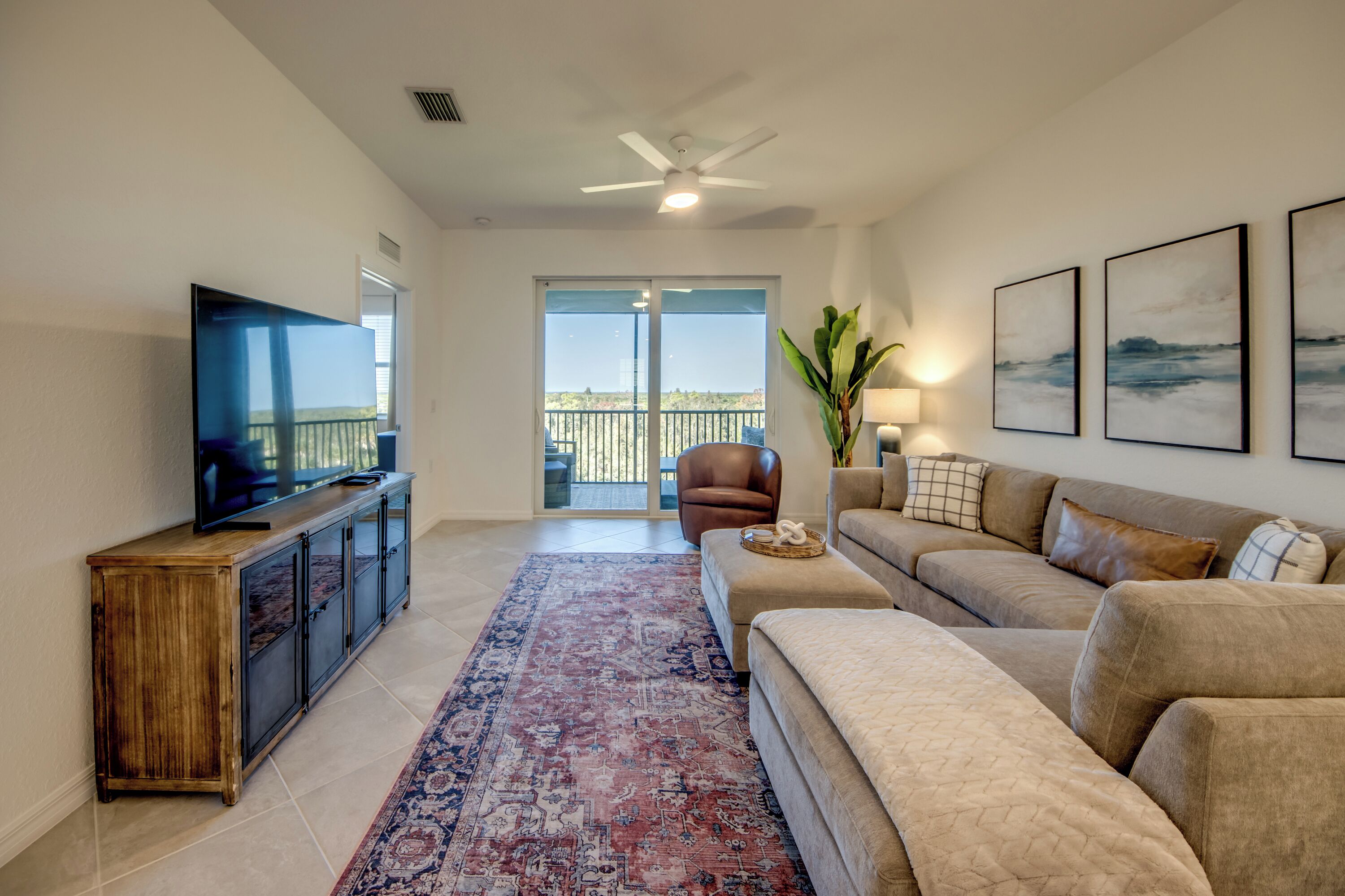 A living room with a television, a sofa, a coffee table, and a large window with a balcony.