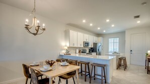 A modern kitchen with white cabinets, a central island, and bar stools. - Modern Heritage Landing Condo – Resort Lifestyle (Punta Gorda)