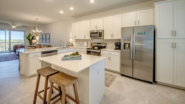 A modern kitchen with white cabinetry, stainless steel appliances, and a large island with stools. - Modern Heritage Landing Condo – Resort Lifestyle (Punta Gorda)