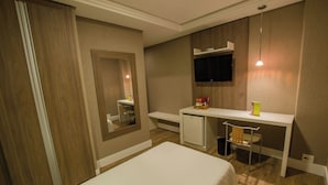 Een hotelkamer met een bed, een bureau met stoel, een aan de muur bevestigde televisie en een klein kastje.