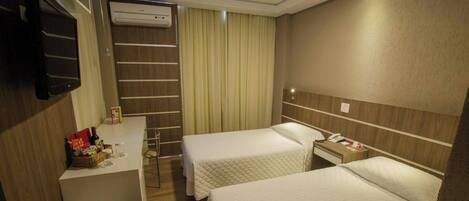 A hotel room with two beds, a desk with a chair, a minibar, and a TV mounted on the wall.