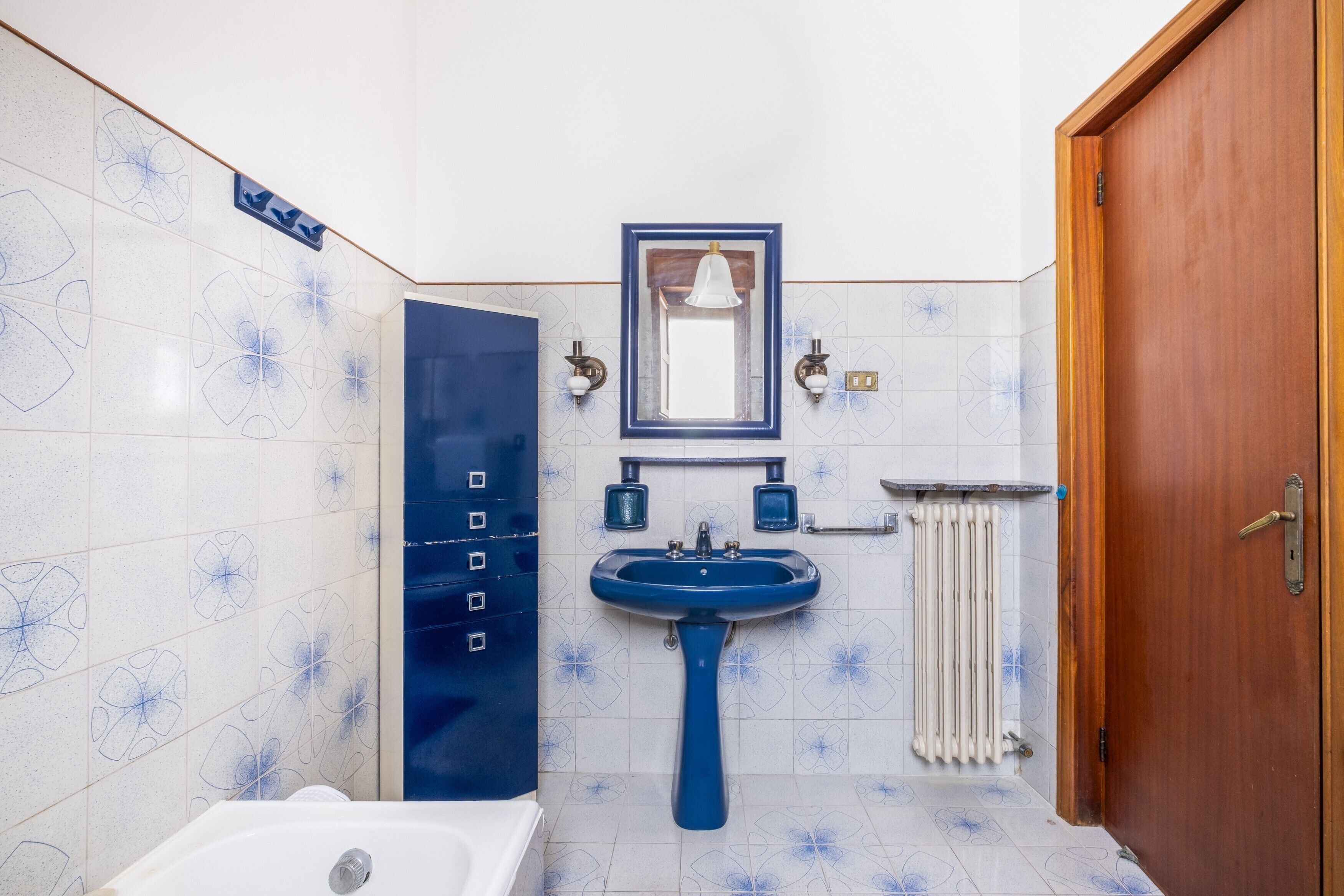 Une salle de bain avec un lavabo bleu, un miroir, un porte-serviettes et une porte.