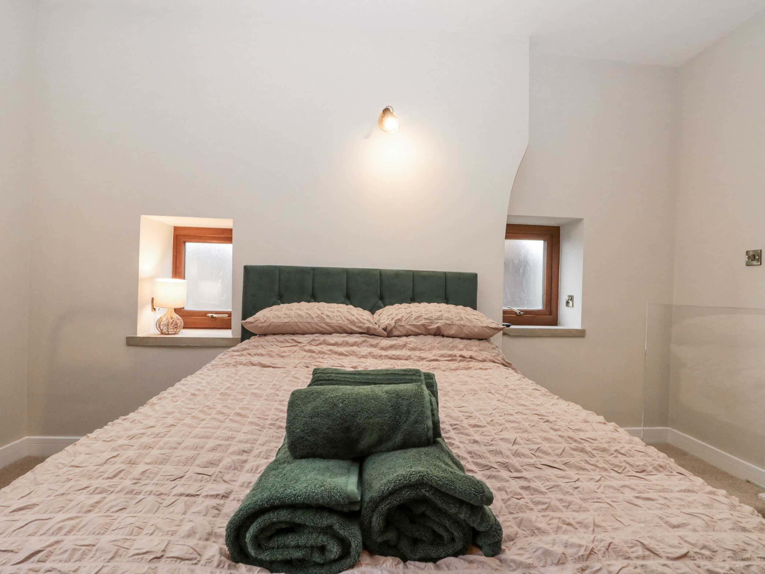 A bedroom with a bed, two windows, and a wall-mounted light fixture.
