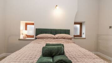 Un dormitorio con cama, dos ventanas y una lámpara fijada a la pared.