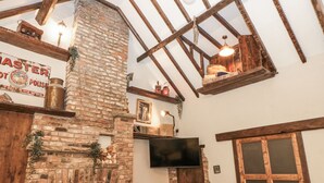 Una habitación rústica con vigas de madera a la vista, una chimenea de ladrillo y un televisor montado.