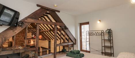 A bedroom with a loft area, a bed with a white textured duvet, a glass-walled seating area, and a wooden staircase.