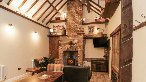 Una habitación acogedora con chimenea de ladrillo, vigas de madera, una mesa de comedor y un rincón de descanso confortable.