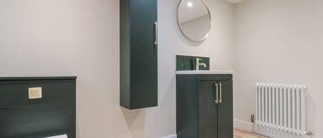 Une salle de bain avec des toilettes, un meuble sombre doté d’un miroir et un radiateur.
