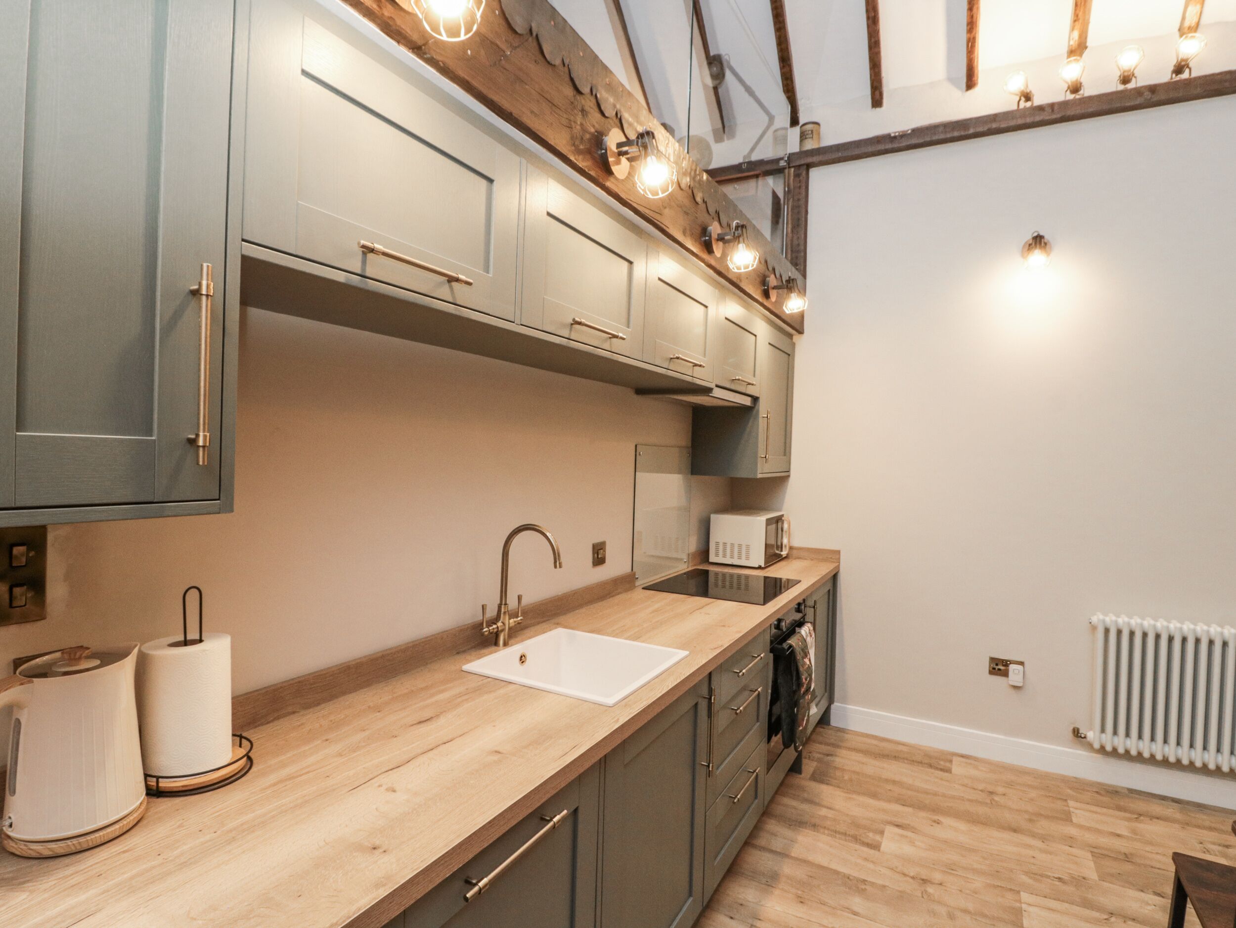 A modern kitchen with grey cabinets, a wooden countertop, and a built-in microwave.