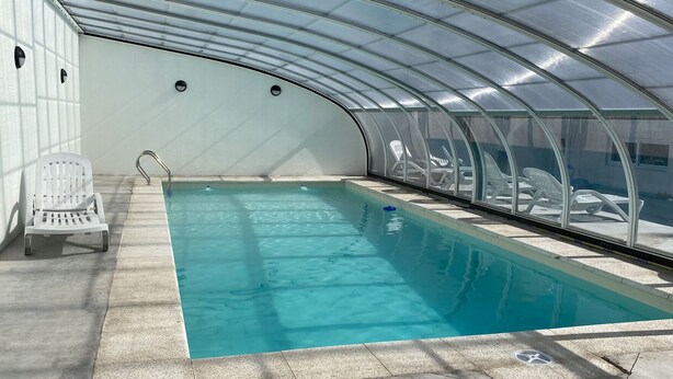 Une piscine intérieure à l’eau claire, entourée de chaises longues et dotée d’un toit en verre.