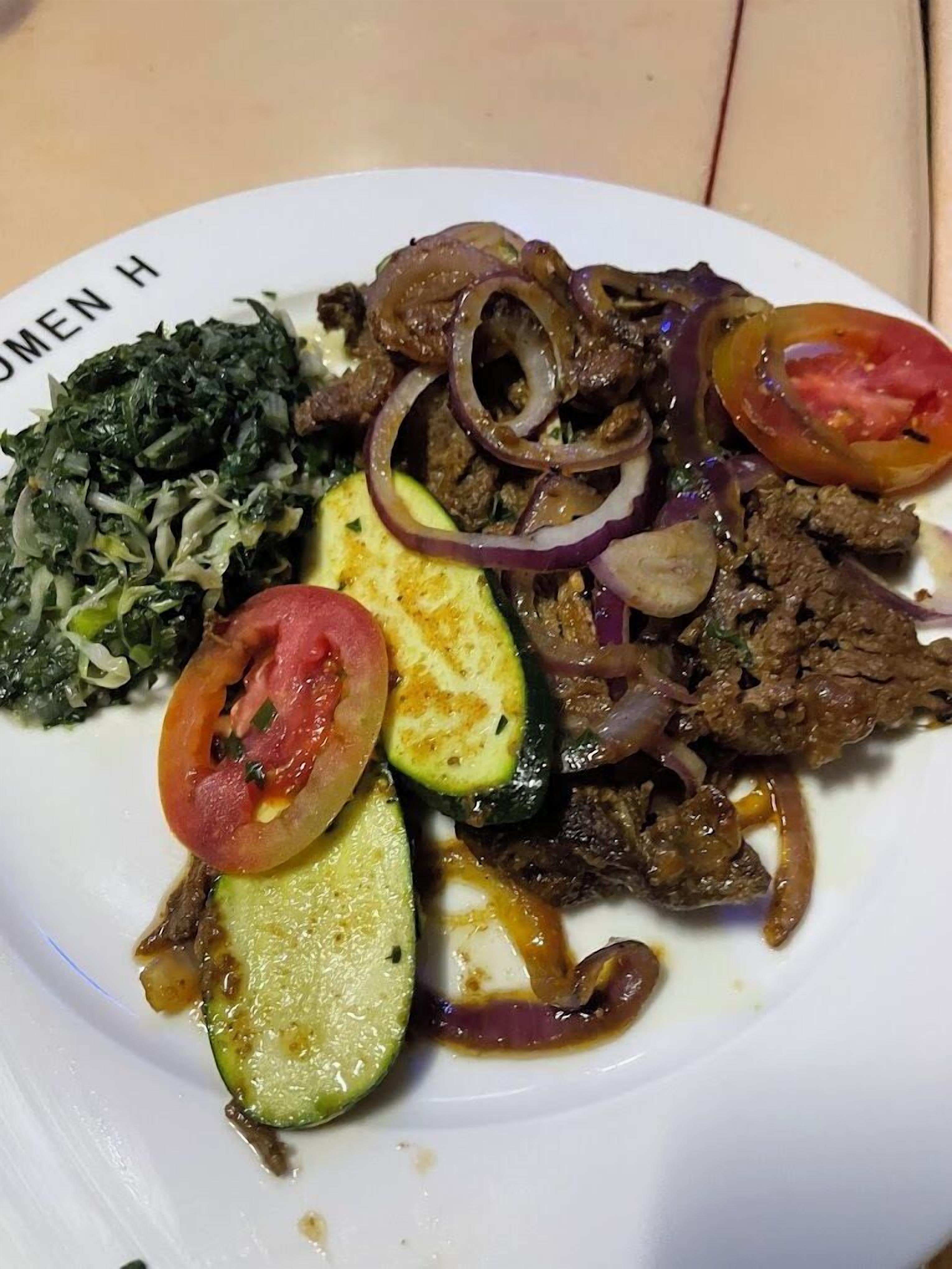 A plate of food with beef, onions, tomatoes, and zucchini.