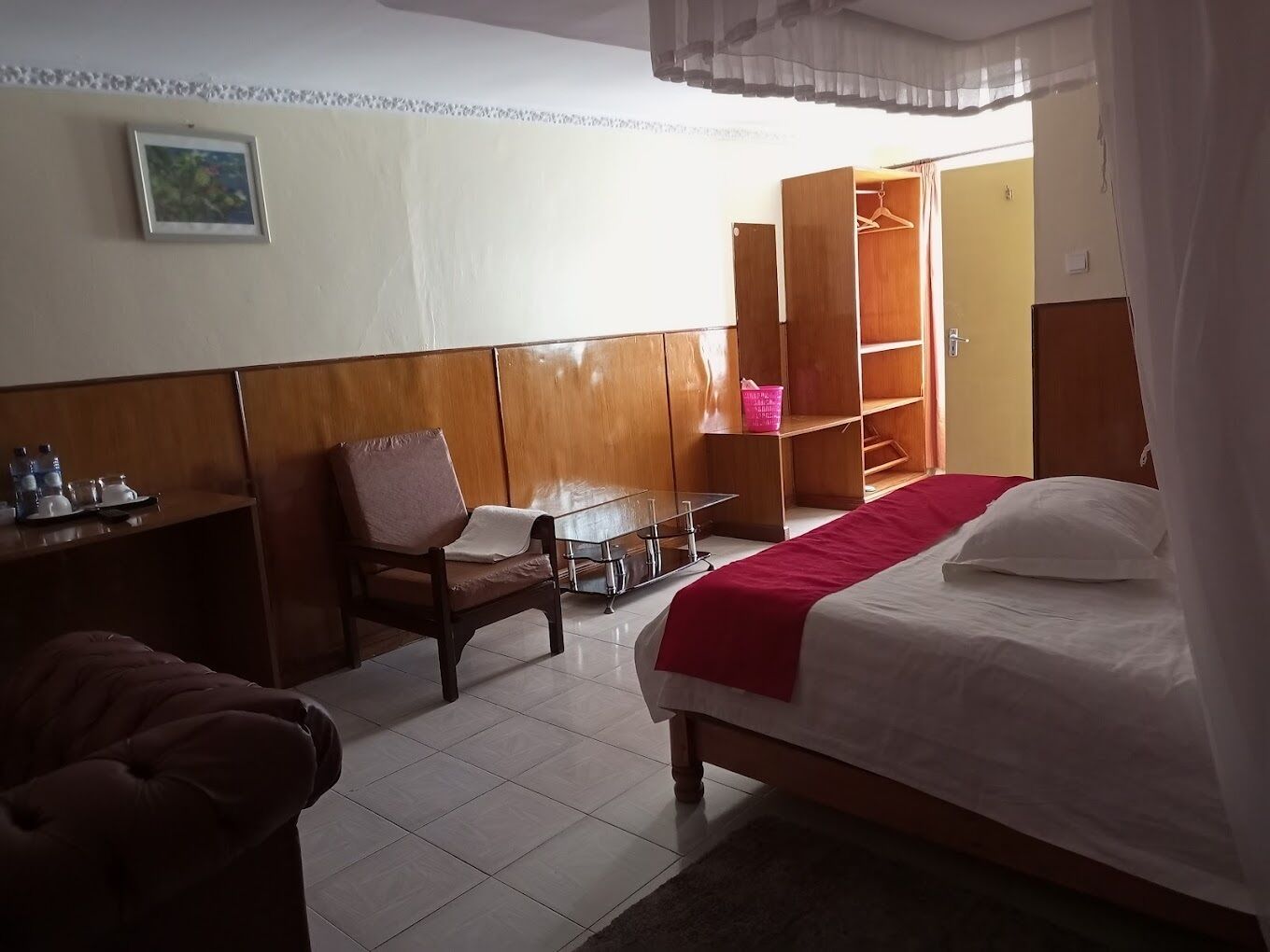 A hotel room with a bed, a desk, a chair, a small table, and a wardrobe.
