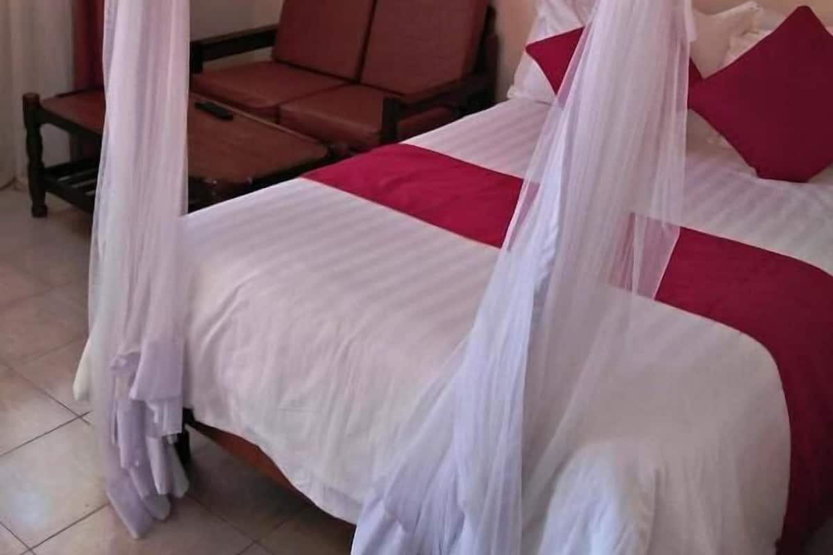 Une chambre avec un lit recouvert d’un dais blanc, une couvre-lit rouge et blanche, et un canapé marron.