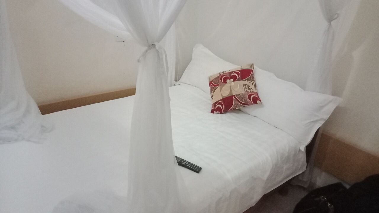 A bed with a white bedspread, a decorative pillow, and a remote control on the side.