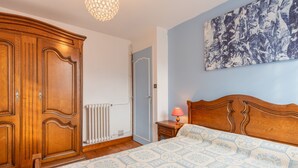 Un dormitorio con un armario de madera, un radiador, una mesita de noche con lámpara y una cama con colcha estampada.
