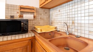 Una cocina con un lavamanos, microondas, armarios de madera y salpicadero de azulejos.
