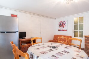 A compact room with a dining table, chairs, a refrigerator, a television, and a painting on the wall. - Panoramic South-Facing Apartment with Mountain Views (Grust)