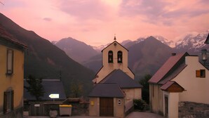 Un pueblo de montaña con una iglesia, edificios de piedra y una vista despejada de montañas nevadas.