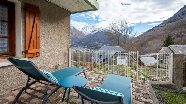 Un balcón con dos sillones de descanso y una mesa, con vistas a un paisaje montañoso y cielo despejado.