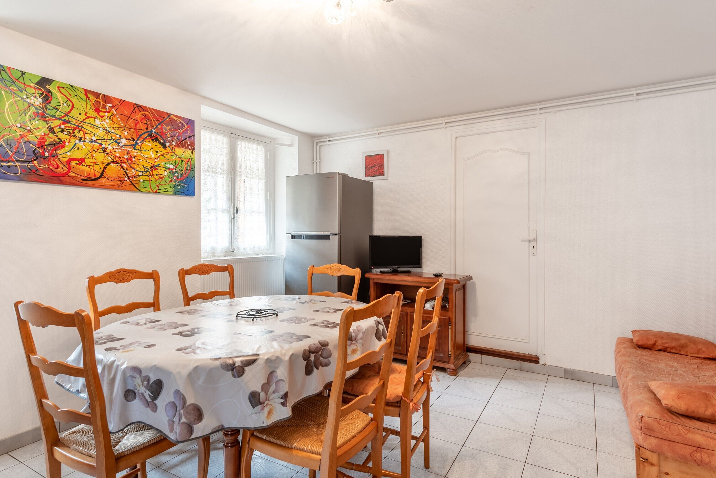 A dining area with a table and chairs, a television, and a colorful abstract painting on the wall.