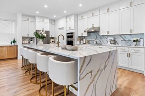 A modern kitchen with white cabinetry, a marble island, and gold accents. - 9BR house with game room near Disney area (Kissimmee)