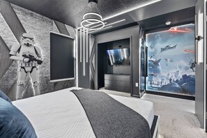 A modern bedroom with a large bed, a Star Wars-themed wall, a flat-screen TV, and a wall mural of space scenes. - 9BR house with game room near Disney area (Kissimmee)