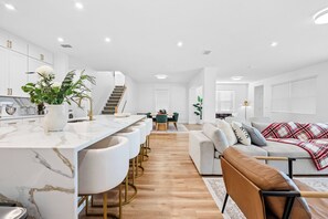 A modern kitchen with white cabinets and a marble countertop, a dining area with a table and chairs, and a living room with a sofa and a coffee table. - 9BR house with game room near Disney area (Kissimmee)