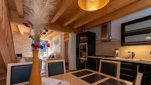 Eine moderne Küche mit Holzbalken, ein Essbereich mit Glastisch und ein gemütlicher Wohnraum mit Kamin.