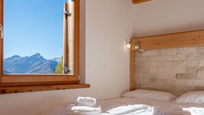 Ein Schlafzimmer mit einem hölzernen Kopfteil, einem großen Fenster mit Blick auf die Berge und ordentlich gefalteten Handtüchern auf dem Bett.