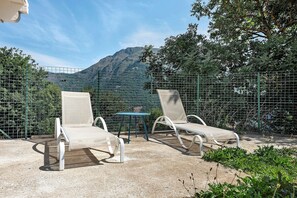 Deux fauteuils de jardin avec une table, une clôture en métal et un paysage montagneux en arrière-plan.
