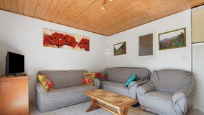 Ein Wohnzimmer mit grauem Sofa, einem Holztisch und einem Fernseher auf einem Schrank.