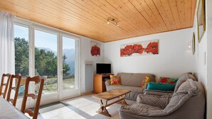 Ein Wohnzimmer mit Holzboden, einer Couch, einem Fernseher und Bergblick durch große Fenster.