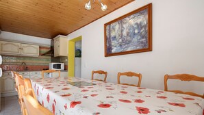 Ein Essbereich mit Tisch für vier Personen, Holzsesseln, einem Gemälde an der Wand und einer Küche im Hintergrund.