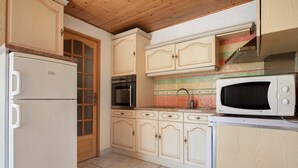 Eine Küche mit Holzschränken, einem Edelstahlbackofen, einer Mikrowelle und einem Kühlschrank.