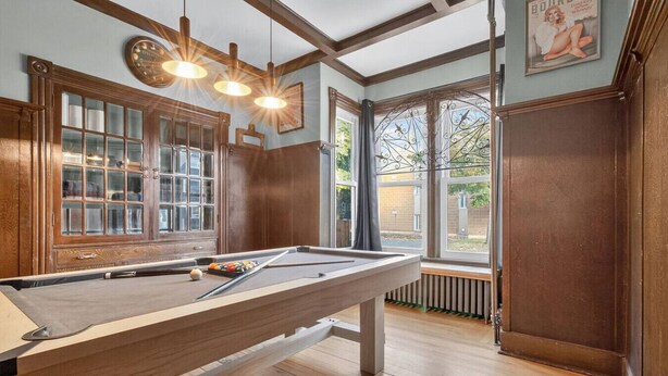 Una mesa de billar en una habitación con suelos de madera y ventanas amplias.