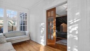 Una habitación con piso de madera, un sofá, una cama y una puerta corrediza de vidrio que da a otra habitación.