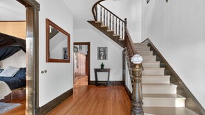 Un pasillo amplio con piso de madera que conduce a una escalera con barandilla de madera y pared blanca.