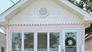 Una casa pequeña de color rosa con una puerta blanca, un porche y una escalera que sube a la puerta.