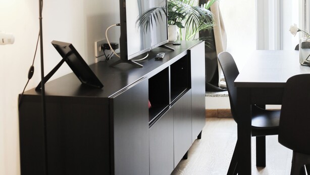 A modern living room with a flat-screen TV, a black entertainment unit, a dining table with chairs, a potted plant, and a large window with curtains. - Cozy Design Apartment in Milan | Piola/Center (Milano)