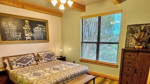 Une chambre à coucher comprenant un lit, un banc en bois, un tapis en peau de vache, un ventilateur de plafond et une fenêtre avec des stores.