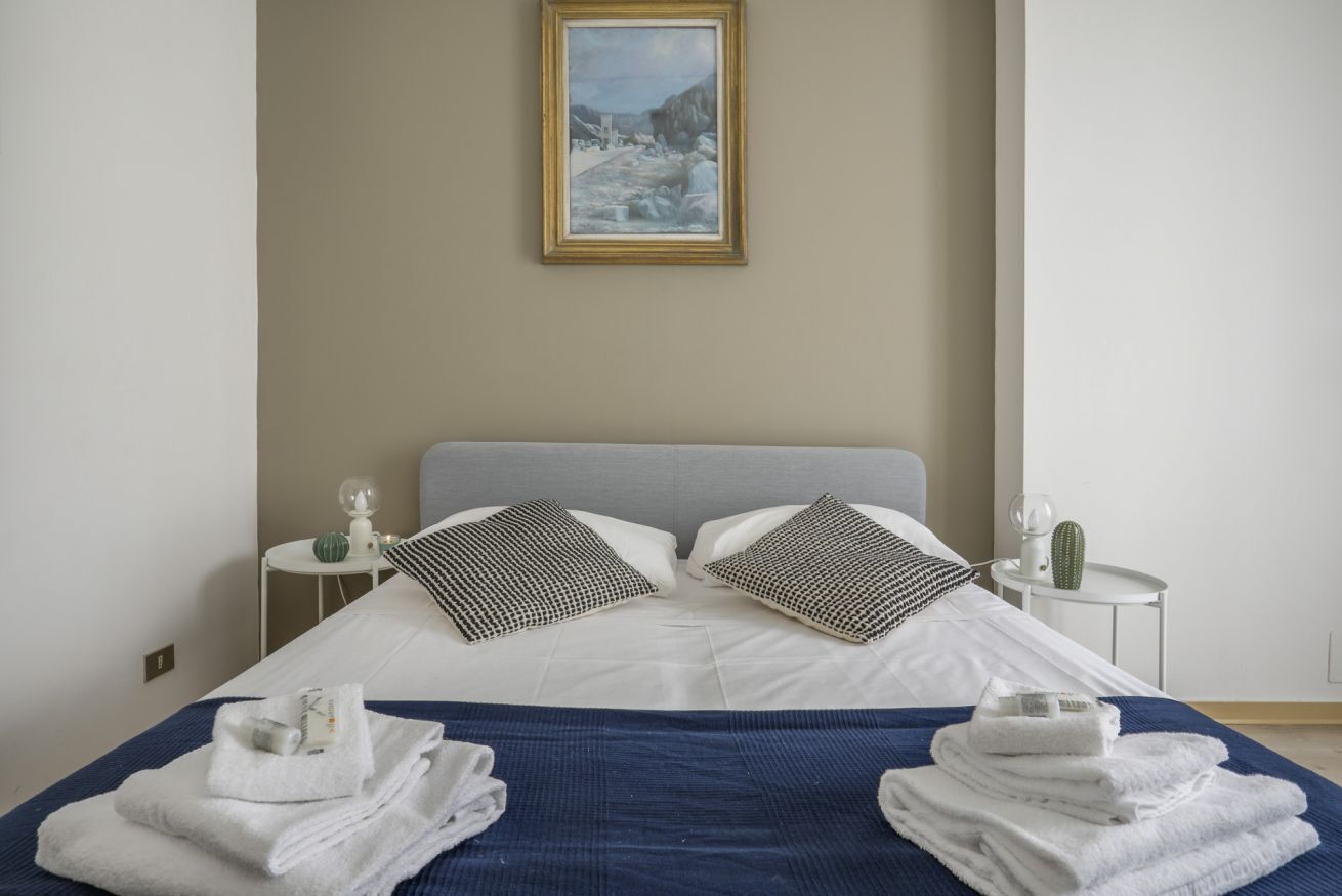 Une chambre d’hôtel avec un lit, des oreillers, un tableau encadré au mur, une petite table avec un cactus et des serviettes sur le lit.