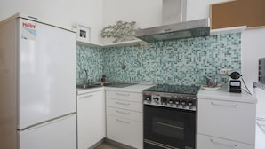 Eine kleine Küche mit weißen Schränken, einem eingebauten Backofen, einem Herd und einer gefliesten Spritzschutzwand.