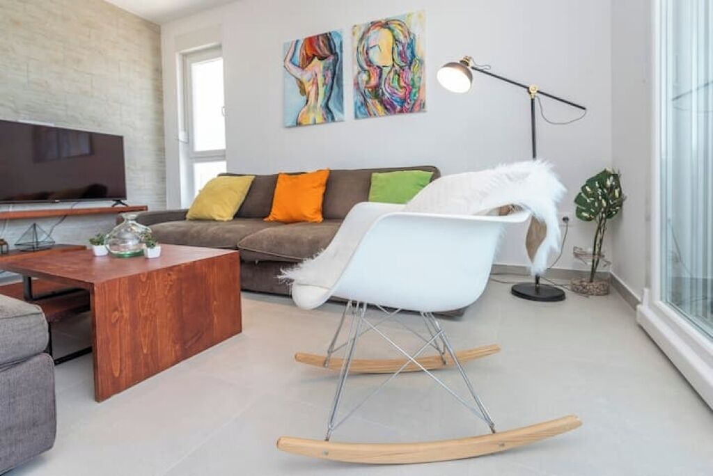 A modern living room with a sofa, a rocking chair, a coffee table, and a flat-screen TV.