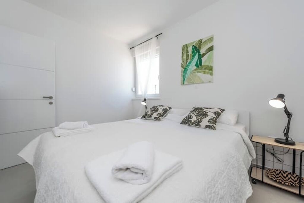 Een net opgemaakt bed met een gevouwen handdoek, een bedlampje en een aan de muur hangend kunstwerk.