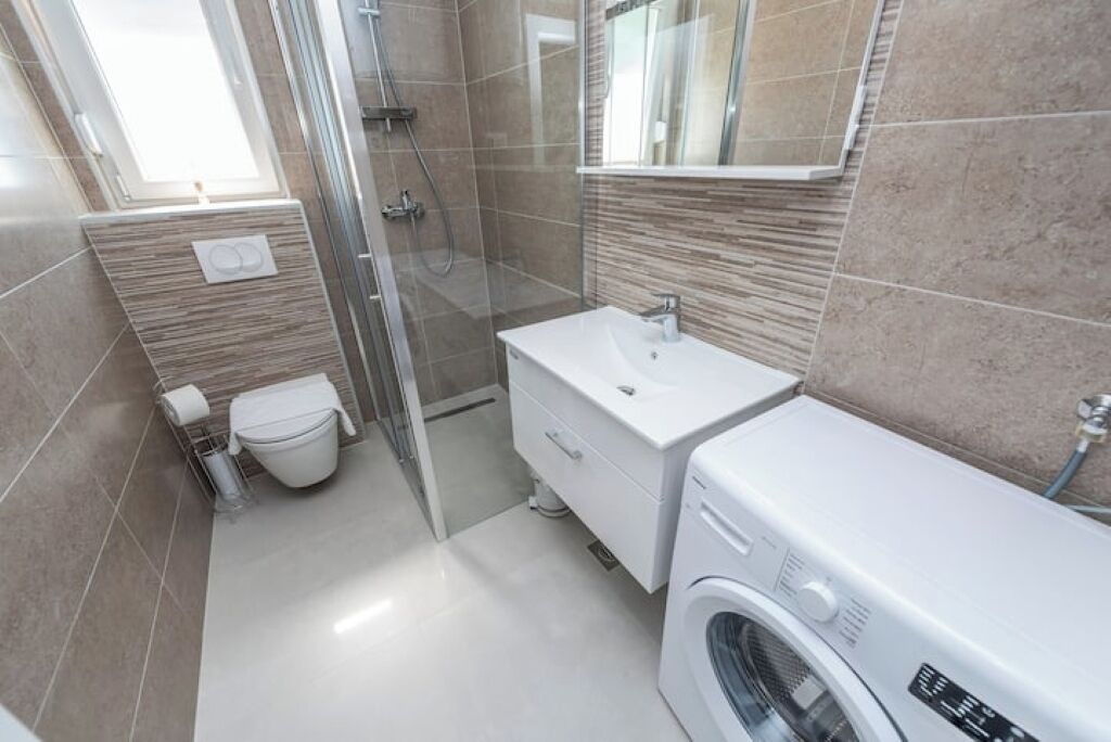 Un baño moderno con cabina de ducha de vidrio, un lavamanos blanco y lavadora integrada.