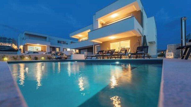 Una moderna casa a due piani con piscina e area salotto esterna.