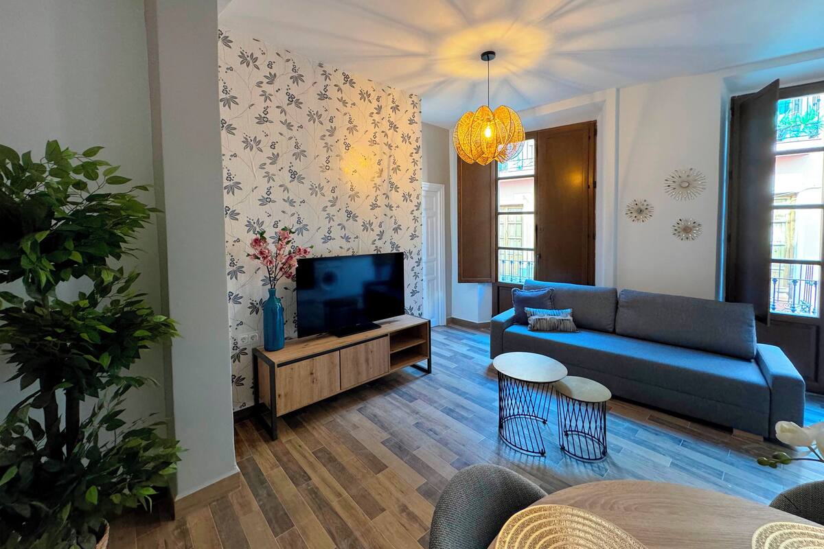 Ein modernes Wohnzimmer mit Flachbildfernseher, grauem Sofa, Couchtisch und einer Pendelleuchte.