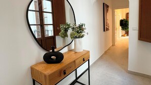 A hallway with a wooden console table, a large mirror, and a potted plant. - Apartamentos Plaza San Agustin 3000 (Granada)