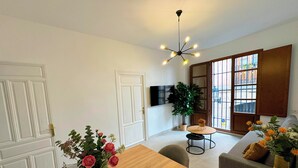 A modern living room with a wooden dining table, a sofa, and a large window with a view. - Apartamentos Plaza San Agustin 3000 (Granada)