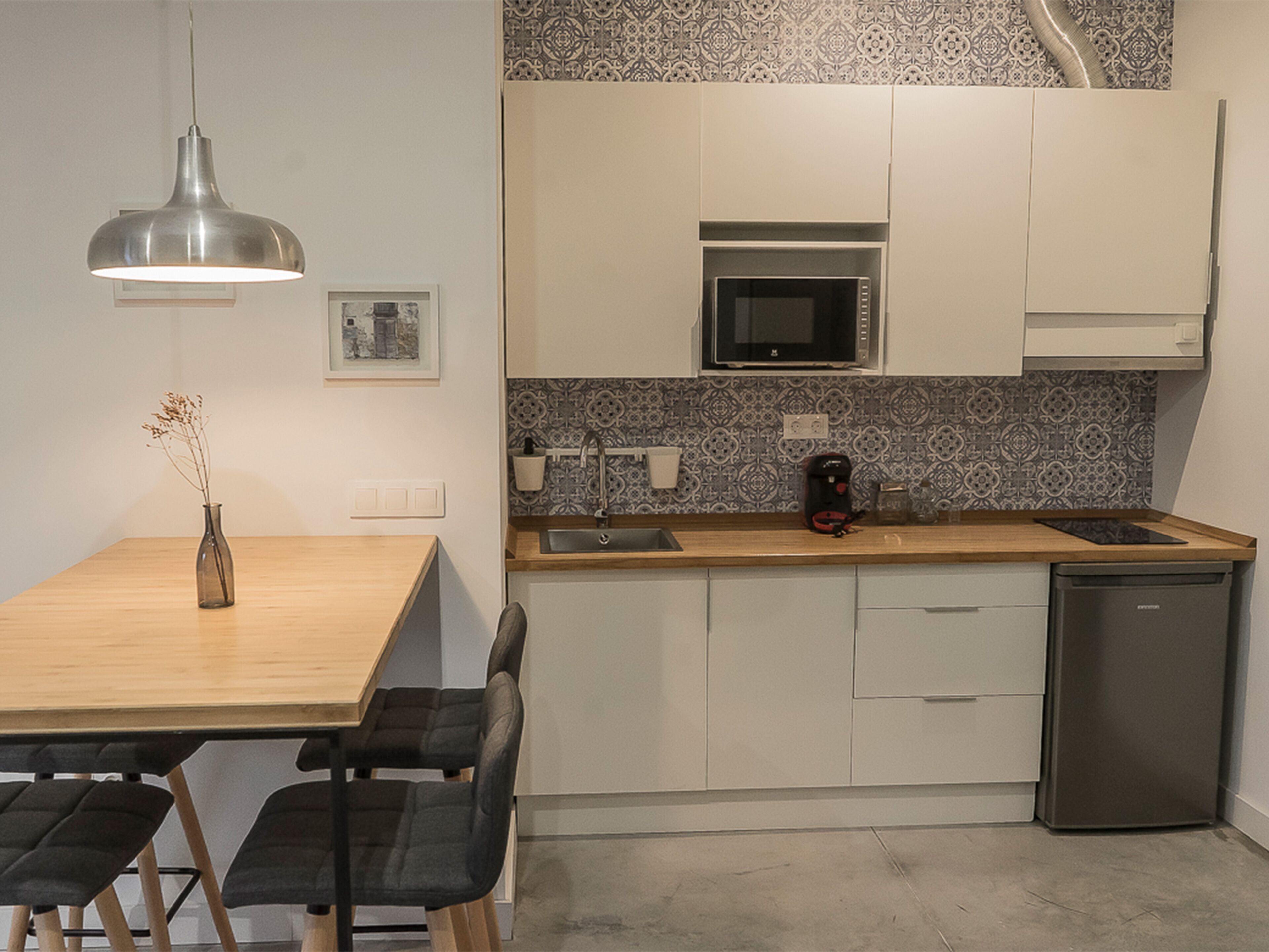 Una cocina moderna con una mesa de madera, sillas negras, microondas, lavaplatos y fregadero.